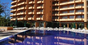 Ein Hotel mit großem Pool, Außenbereich zum Sitzen und mehreren Balkonen.