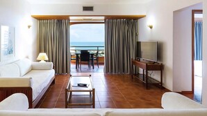 Habitación de hotel con sofá, mesa de centro, televisor y balcón con vistas al mar.