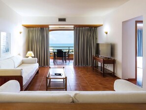 Ein Hotelzimmer mit Sofa, Couchtisch, Fernseher und einem Balkon mit Meerblick.