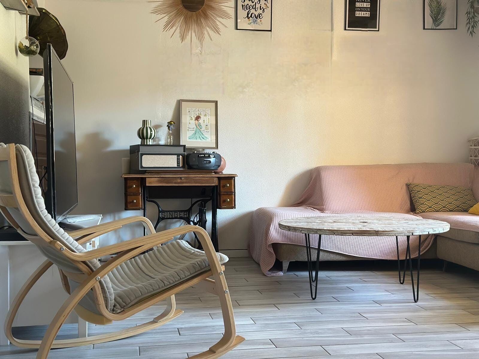 Ein Zimmer mit Schaukelstuhl, einem alten Radio, einem gerahmten Bild, einem rosa Sofa und einem kleinen runden Tisch.