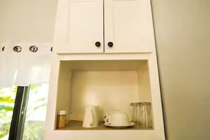 Ein weißes Schränkchen mit zwei Türen, eine Kaffeemaschine, eine Tasse und ein Glas auf einer Arbeitsplatte.