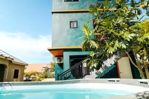 Ein Schwimmbecken mit einer Treppe, die zu einem Gebäude mit blauer Fassade und einem kleinen Fenster führt.
