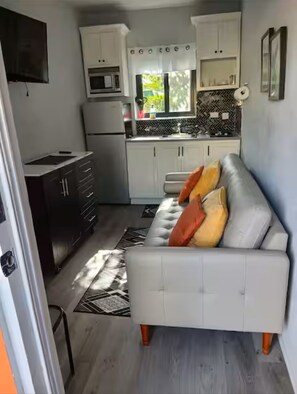 Ein kompakter Wohnraum mit einer Küchenzeile, einer Couch mit Kissen und einem gemusterten Teppich.
