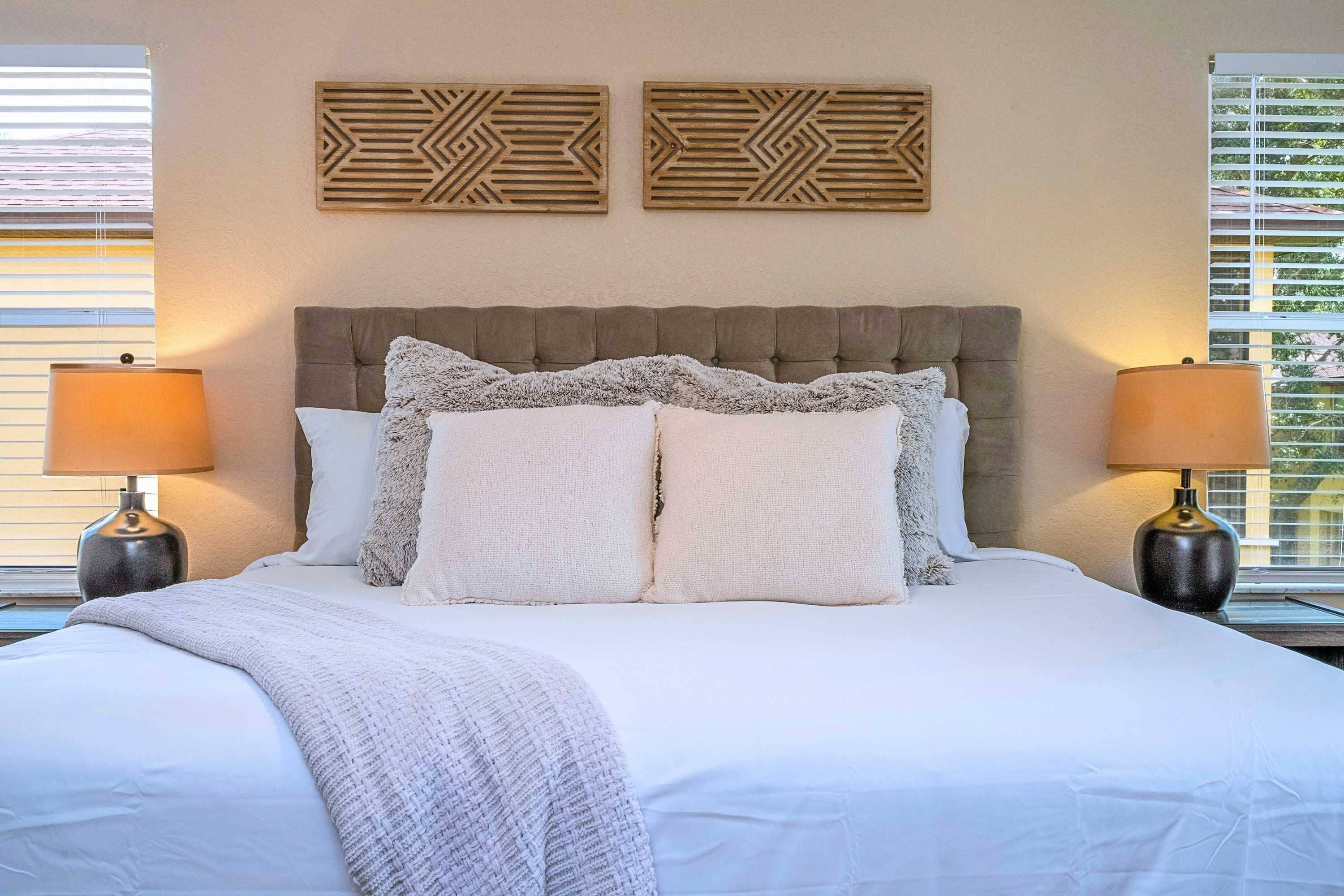 Una cama bien hecha con cabecera capitonada, dos lámparas de noche y paneles decorativos en la pared.