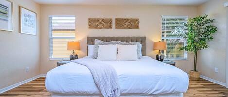 A bedroom with a large bed, two bedside tables, a ceiling fan, and a potted plant.