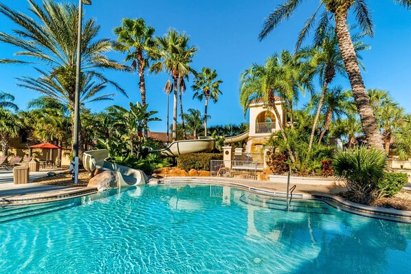 Una piscina con palmeras, un tobogán acuático y un edificio con una entrada arqueada.