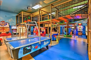 Ein Indoor-Spielbereich mit Tischtennisplatte, Spielhallenspielen und einer mehrstöckigen Spielkonstruktion.