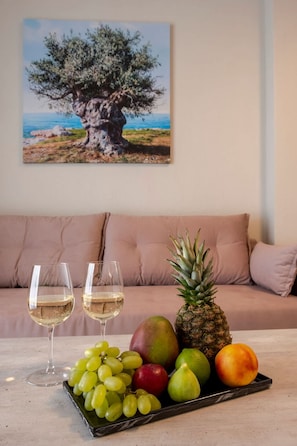 Ein Tisch mit einer Obstschale, zwei Weingläsern und einem Baumgemälde an einer Couch.