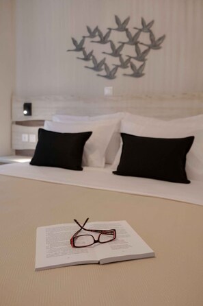 A neatly made bed with black and white pillows, a wall art of birds, and a book with glasses on a bedside table. - Casale Luxury House III - Secret Garden Maisonette (Sithonia)
