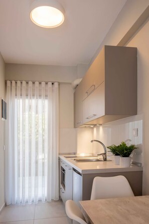 A compact kitchen with a built-in oven, a sink, and a dining area with a table and chairs. - Casale Luxury House III - Secret Garden Maisonette (Sithonia)