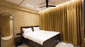 A modern bedroom with a large bed, a round mirror, a ceiling fan, and a window with curtains.