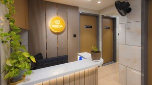 A reception desk with a sign reading 'NIRRTUL The Natural Way,' a potted plant, and a wall-mounted fan.