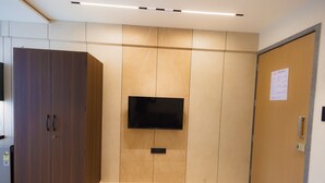 A room with a large wardrobe, a flat-screen TV mounted on the wall, and a door with a welcome sign. - Nirrtul Crystal 1BHK Apartment Cozy & Quite (Surat)