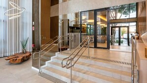 A modern hotel lobby with a staircase, a reception desk, and a view of the outdoor area. - Studio charmoso e bem localizado (São Paulo)