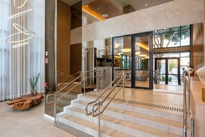 Eine moderne Hotelhalle mit Treppe, Rezeption und Blick ins Freie.