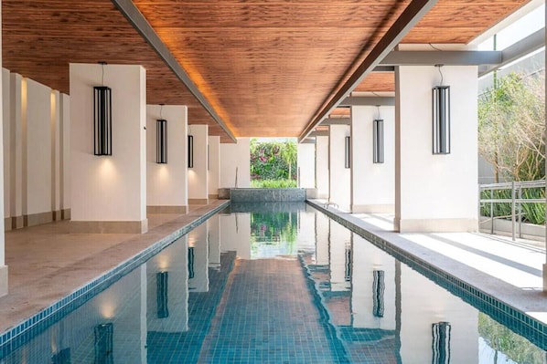 Ein langer, überdachter Schwimmbereich mit Holzbalkendecke und weißen Wänden.