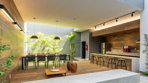 A modern kitchen with a bar area, a dining table with chairs, and a seating area with a bench. - Studio charmoso e bem localizado (São Paulo)