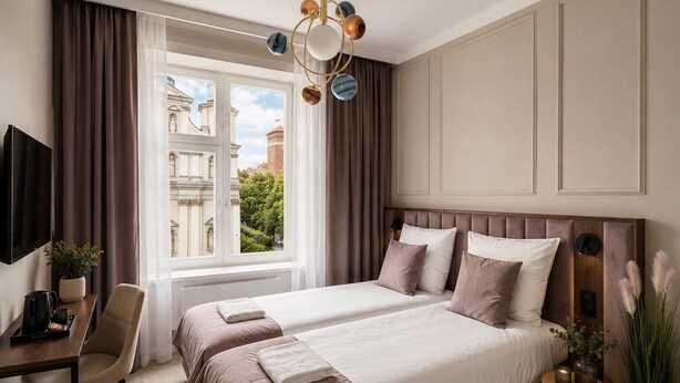 Ein Hotelzimmer mit einem großen Bett, einem Schreibtisch mit Stuhl, einem Fernseher und Blick auf Gebäude vor dem Fenster.