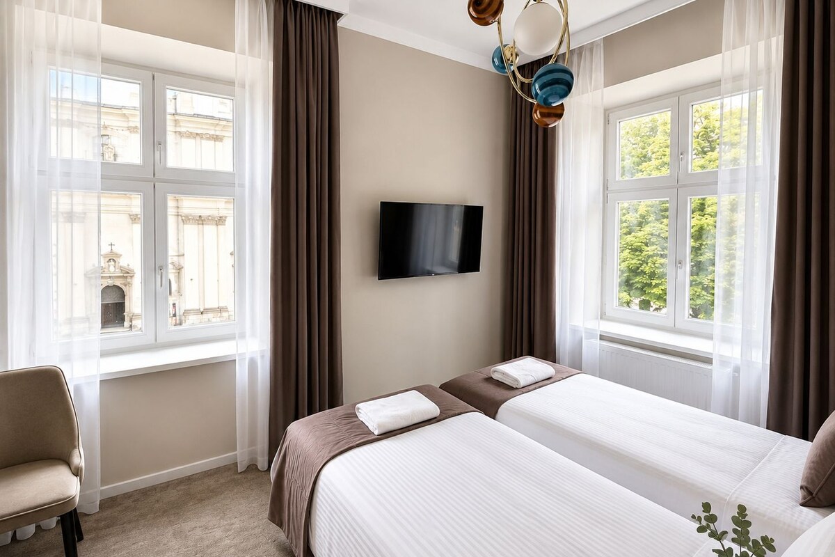 Una habitación de hotel con dos camas, televisión y ventanas amplias con cortinas.