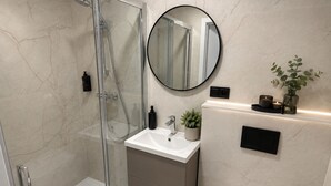 Ein modernes Badezimmer mit einer gläsernen Dusche, einem weißen Waschbecken und einem runden Spiegel.