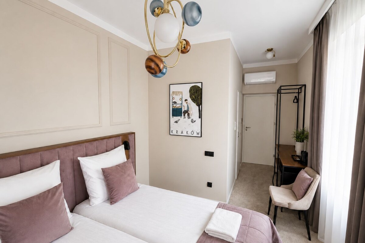 Habitación de hotel con dos camas, un escritorio, una silla, aire acondicionado instalado en la pared y un cuadro enmarcado.