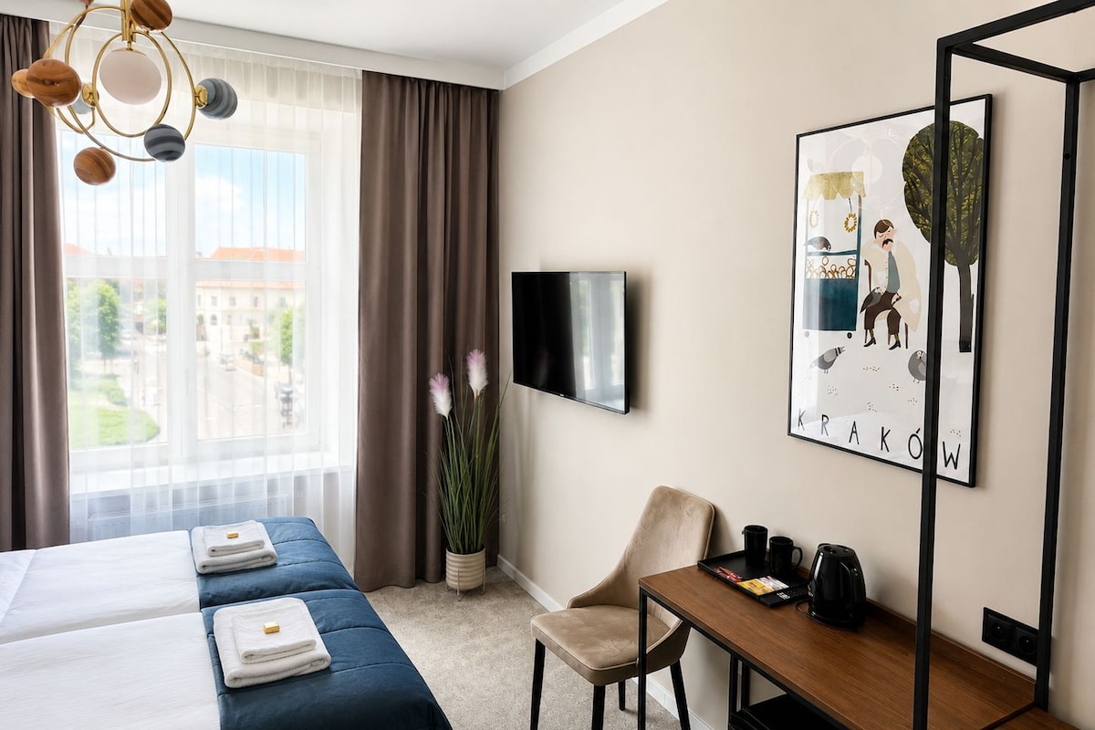 A hotel room with a bed, a desk, a chair, a TV, and a window with curtains.
