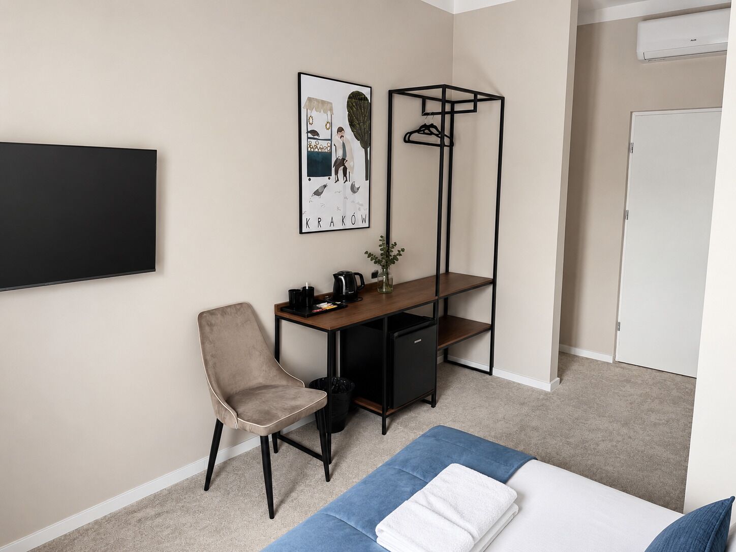A bedroom with a bed, a desk with a chair, a hanging shelf, and a wall-mounted TV.