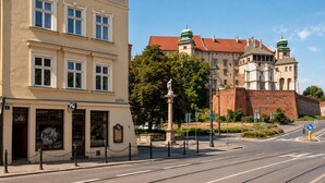 Eine Straße mit einem Gebäude, das eine Statue, eine Straßenbahnlinie und ein Schild mit der Aufschrift 'Best Wine' zeigt.