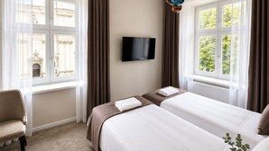 Ein Hotelzimmer mit zwei Betten, einem Fernseher und großen Fenstern mit Vorhängen.