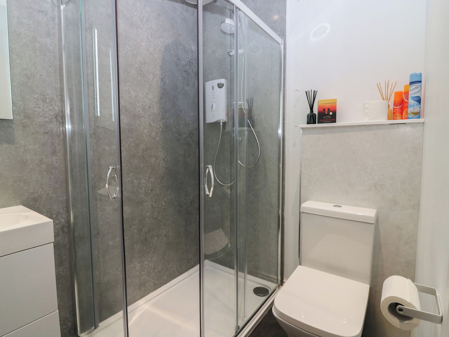 Ein modernes Badezimmer mit einer Duschkabine, einer Toilette und einem Ablagefach für Pflegeartikel.