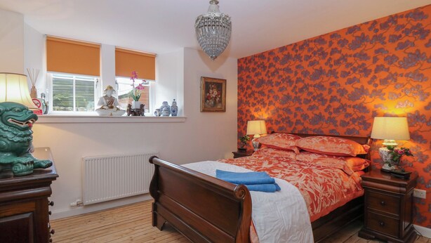 Un dormitorio con una cama de madera, dos mesitas de noche con lámparas, una ventana con persianas, un radiador y una estatua decorativa de león verde.
