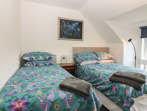 A bedroom with two beds, each with floral-patterned bedding, a framed artwork on the wall, and a nightstand with a lamp. - Luxury Old School (Peebles)
