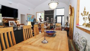 Un comedor con una mesa de madera, sillas, una araña y un televisor.