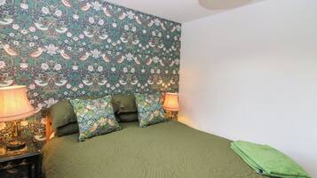 A bedroom with a floral wallpaper, green bedding, two bedside lamps, and a green towel on the bed.