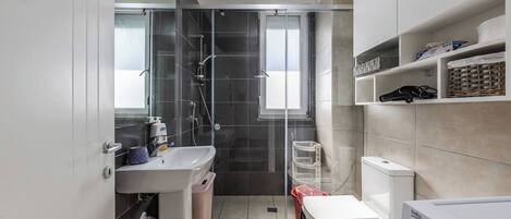 A modern bathroom with a glass shower enclosure, a sink with a soap dispenser, a toilet, and a washing machine.