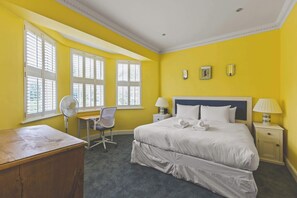 A hotel room with a large bed, a desk, a chair, and a window with blinds.