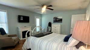 Une chambre à coucher comprenant un lit, un ventilateur de plafond, une télévision, une cheminée, une commode, une chaise et une lampe.