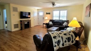 Un salon avec un canapé, une table basse, un téléviseur et un ventilateur de plafond.