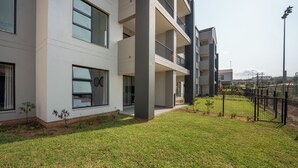 A modern multi-story building with balconies, a well-maintained lawn, and a fenced outdoor area. - Ballito Village Estate (Ballito)