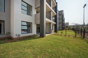 A modern multi-story building with balconies, a well-maintained lawn, and a fenced outdoor area. - Ballito Village Estate (Ballito)