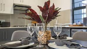 A dining table set with plates, cutlery, and a vase with a plant. - Ballito Village Estate (Ballito)