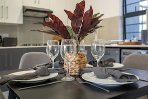 A dining table set with plates, cutlery, and a vase with a plant. - Ballito Village Estate (Ballito)