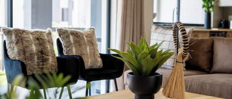 A modern living room with a wooden coffee table, a potted plant, a broom, and two chairs with cushions.