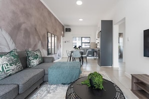 A modern living room with a sofa, a coffee table, and a dining area in the background.