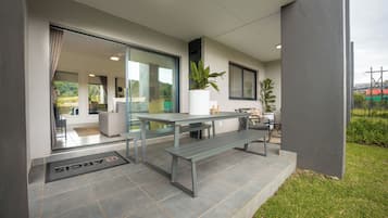A modern outdoor patio with a table and benches, a potted plant, and a glass door leading to an interior space.