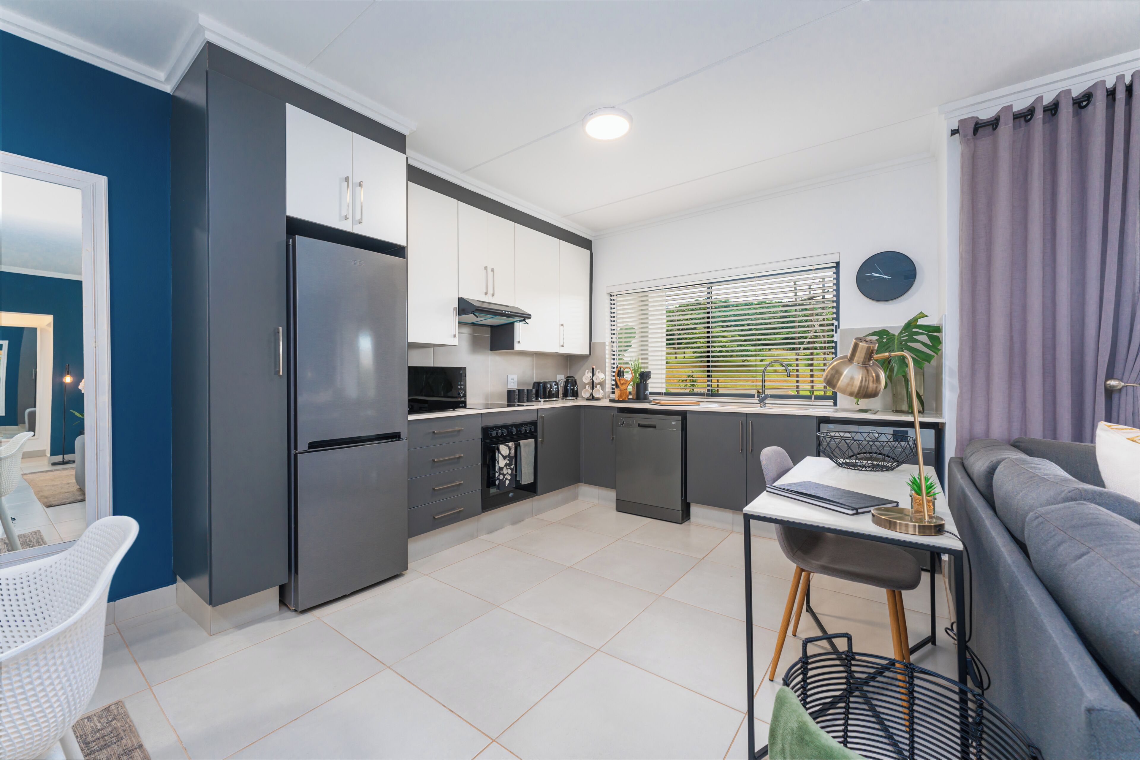 A modern kitchen with grey cabinets, a built-in oven, and a dining area with a table and chairs.