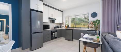 A modern kitchen with grey cabinets, a built-in oven, and a dining area with a table and chairs.