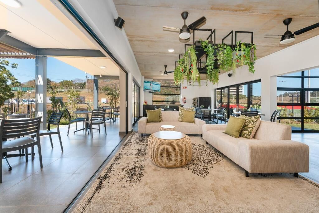 A spacious indoor area with a sofa, chairs, a round wicker table, and hanging plants.