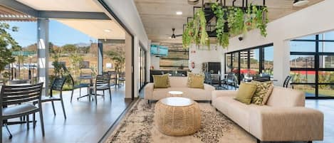 Un espacio interior amplio con un sofá, sillas, una mesa redonda de mimbre y plantas colgantes.