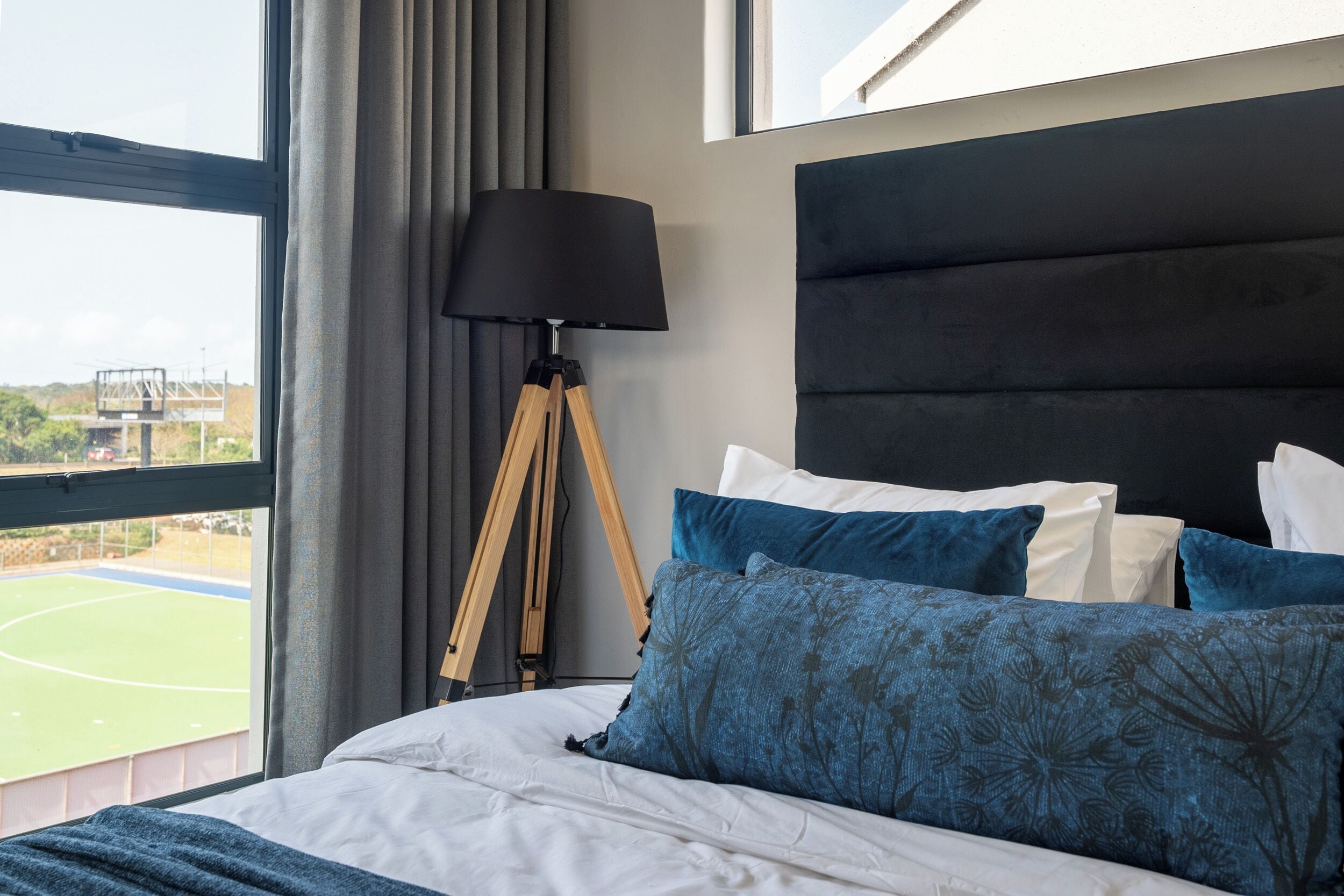 A bed with white and blue bedding, a dark headboard, and a tripod floor lamp.